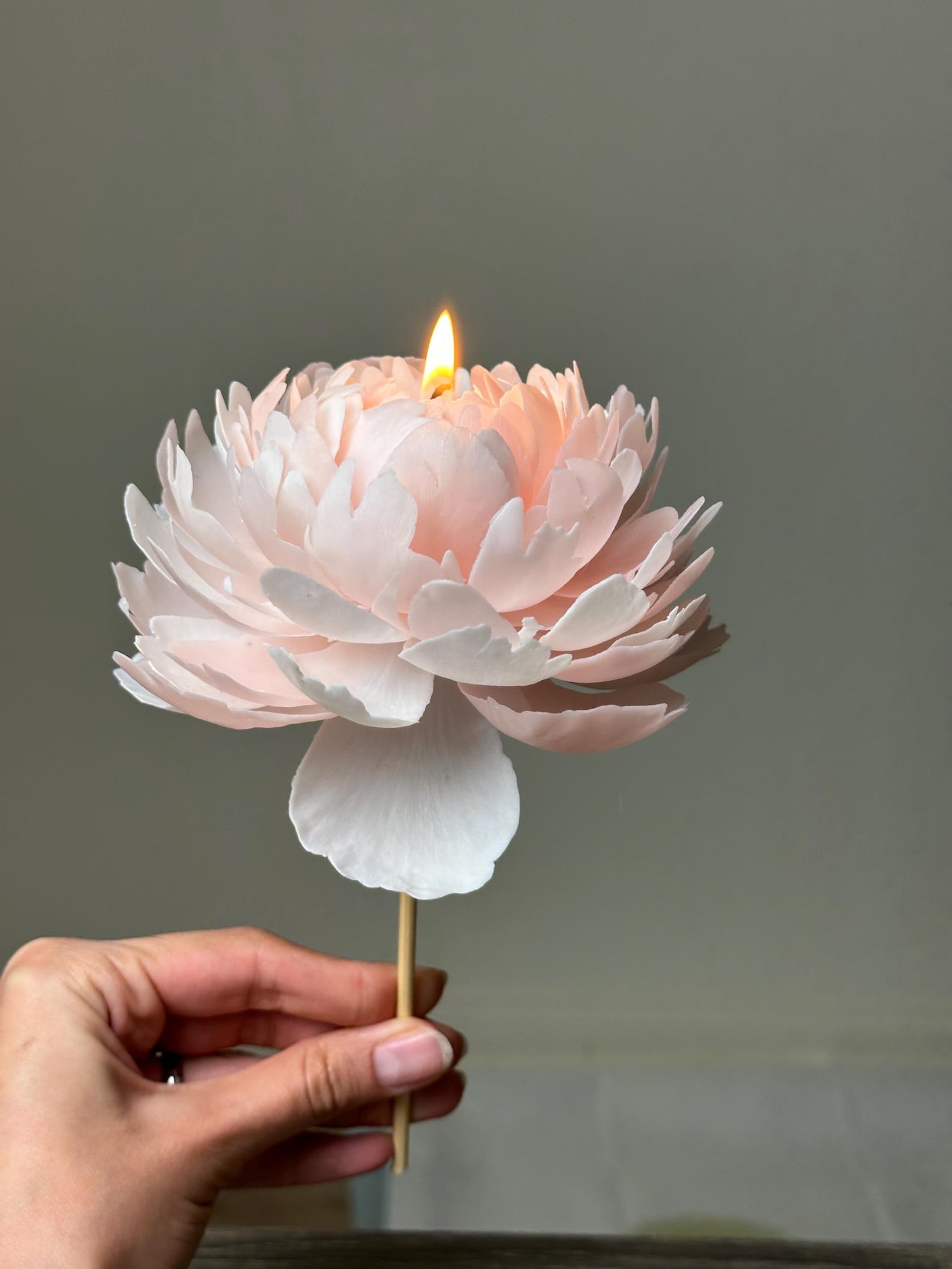 A hand-sculpted, hand-poured peony candle by Eco Candle Lab, lit